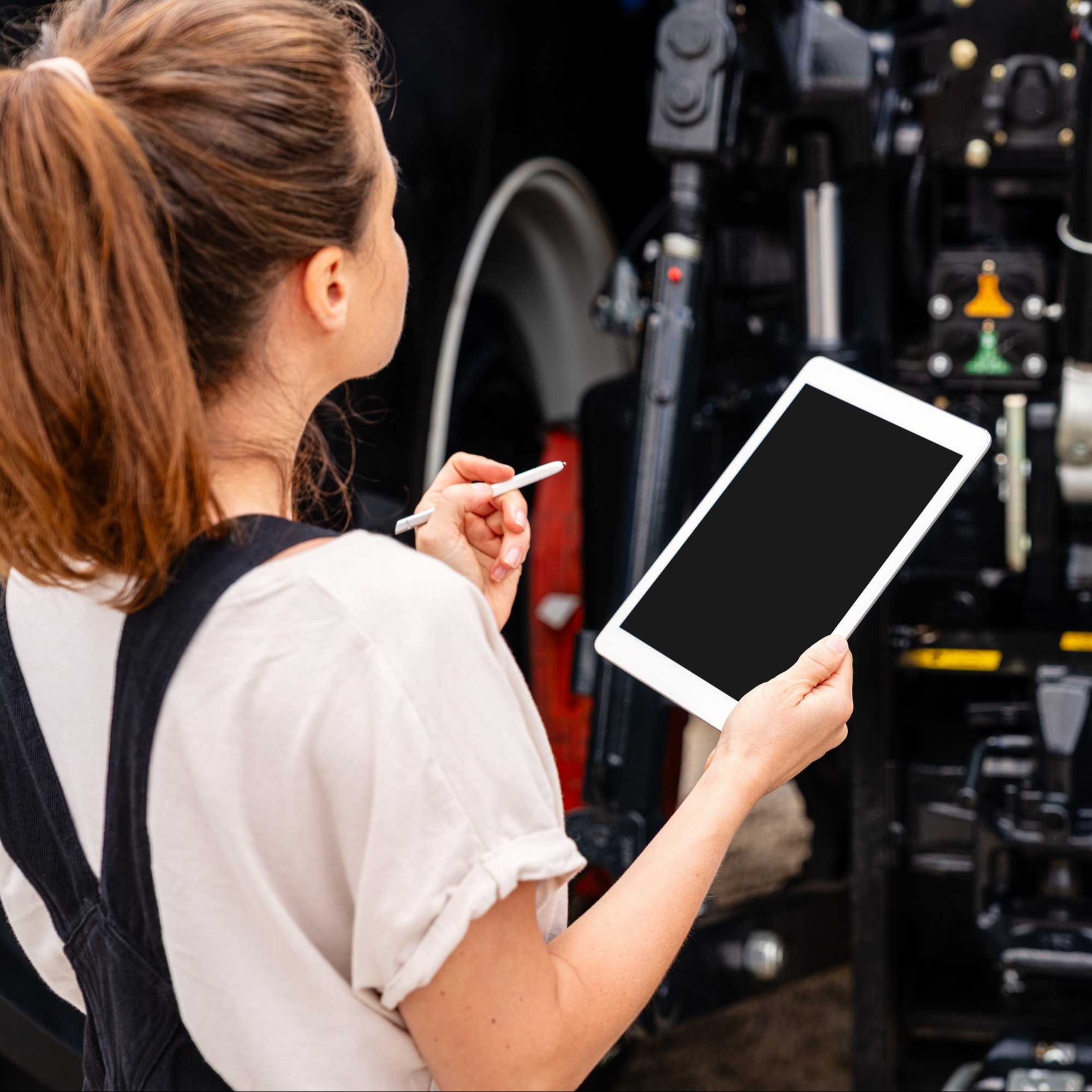 Technikerin inspiziert einen Traktor mit Tablet in der Hand