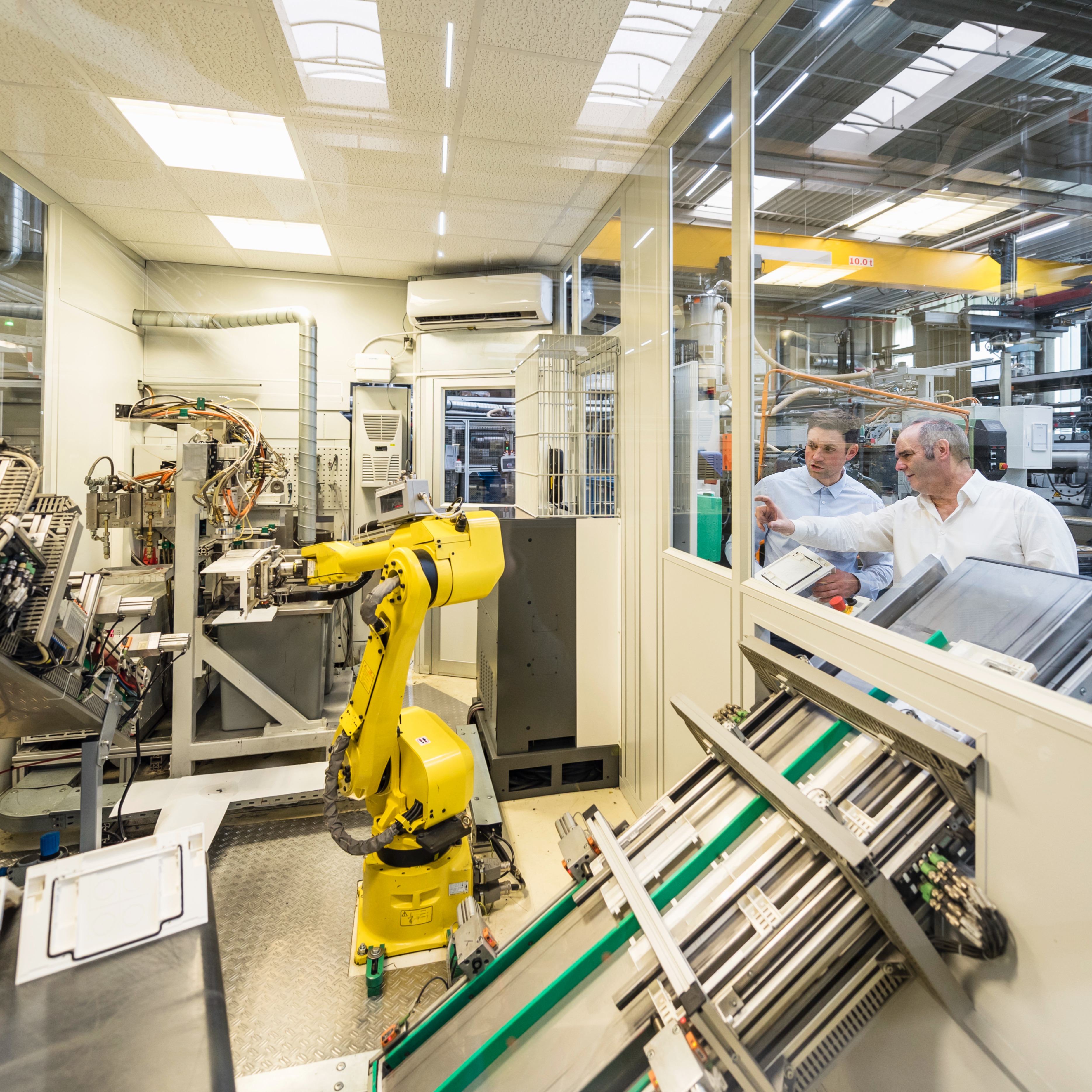 Zwei Männer unterhalten sich in einer Produktionshalle und beobachten einen Roboterarm